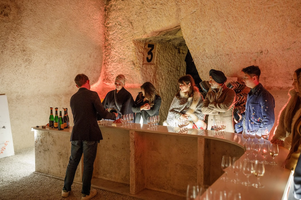 Guests at a candlelit tasting bar in a chalk champagne cellar, glasses lined up along the counter